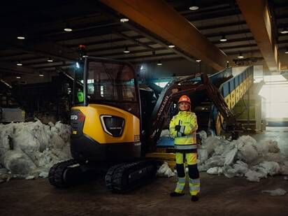 Woman standing next to compact excavator at a recycling facility
